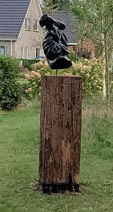 Je ziet een meerpaal met daarop een groot tuinbeeld van een zeehaas. De steen is heel donker en zit vol golvende bewegingen.