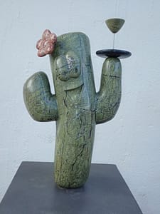 Je ziet een dame in cactusvorm, 2 armen omhoog en een blij gezicht, lichtelijk naar achteren gebogen lichaam. De steen is groen met zwarte lijnen erdoor. Aan de linkerkant op haar hoofd zit een rode bloem, ook van steen gemaakt. Bovenop haar rechterarm heeft ze een dienblad met daarop een glaasje likeur, alles uit steen gemaakt. Het dienblad is zwart en het glaasje is weer de groene steen. Het beeld is het logo van het bedrijf Cadushi Distillery en zij maken likeuren en dranken uit cactus.