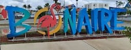 Op de afbeelding staat het woord Bonaire. Hier worden vaak foto's met toeristen gemaakt, het is een kunstwerk bij Isidel park op Bonaire.