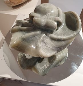 Een octopus in groenige steen. Het beeld zweeft boven een spiegel zodat je ook de zuignappen aan de onderkant kan zien.